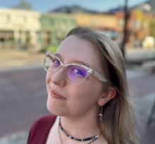 Woman with glasses and blonde hair standing on a sidewalk smiling